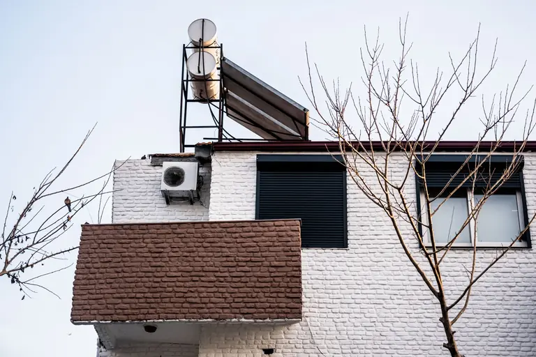 A minimalist building facade with air conditioner and bare winter trees, viewed from a low angle.